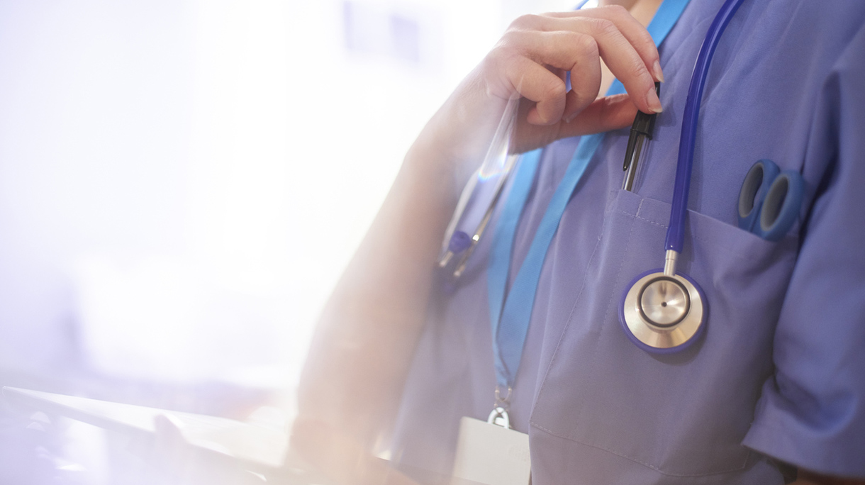 Surgeon using digital tablet in hospital and reaching for her pen