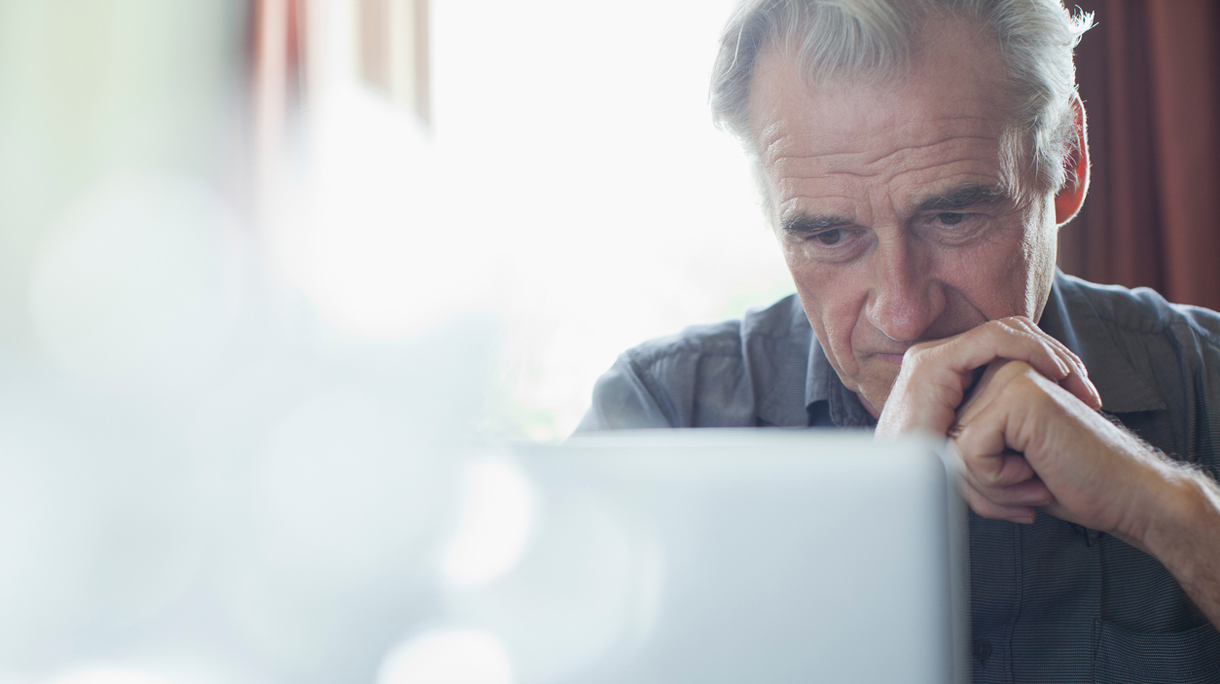 Senior man with hands clasped using laptop