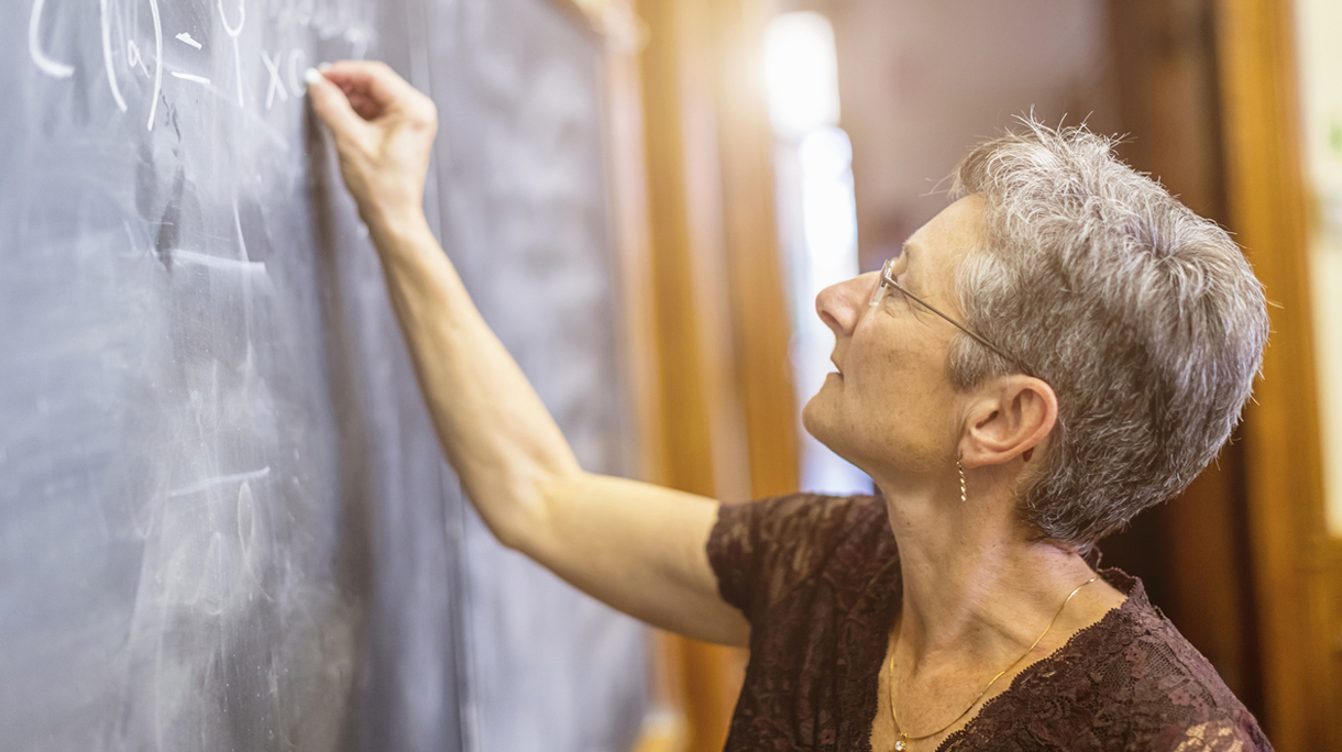 Female Senior Mathemathics Professor at Chalkboard Writing Formula