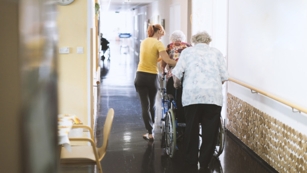 Assistant In The Retirement Community Helping Senior Woman Walking