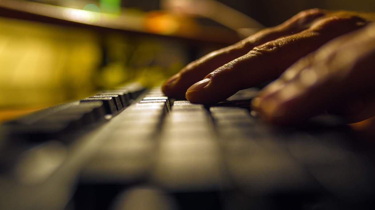 Fingers pressing on a computer keyboard in the dark .