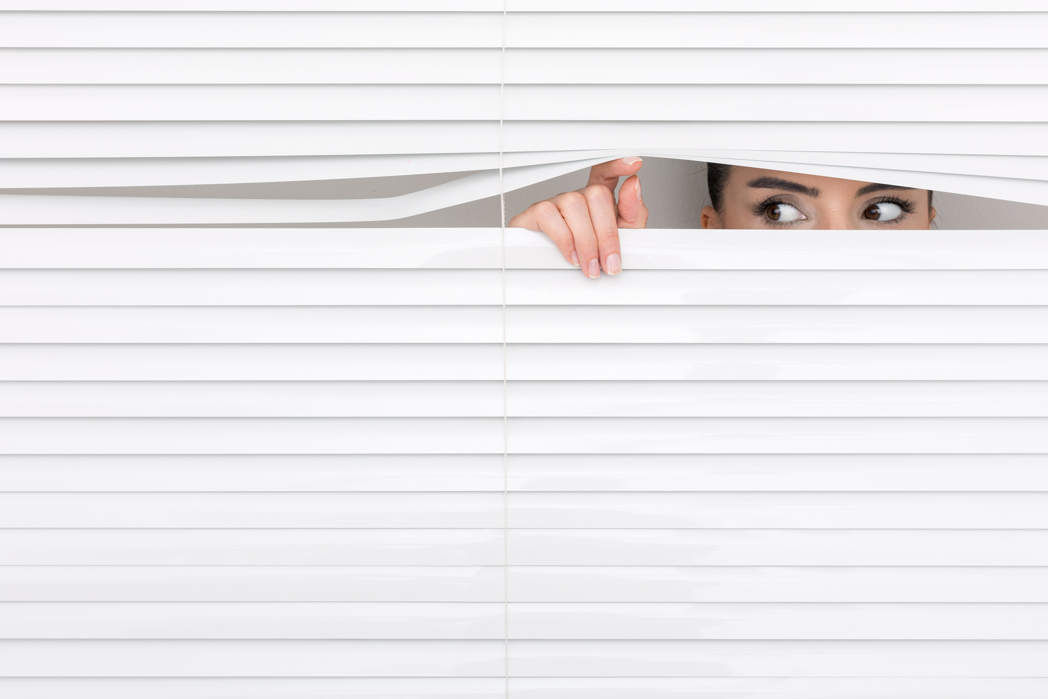 Portrait of a woman looking through out the blinds.