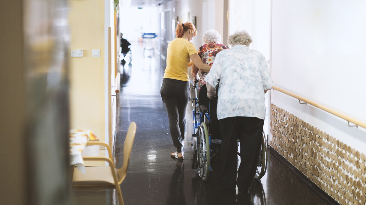 Assistant In The Retirement Community Helping Senior Woman Walking