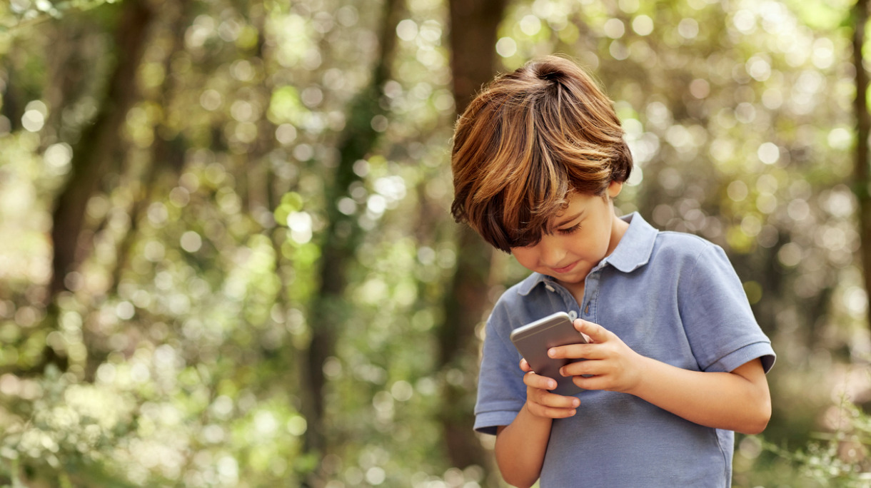 smiling-boy-using-mobile-phone-in-forest-picture-id800433360