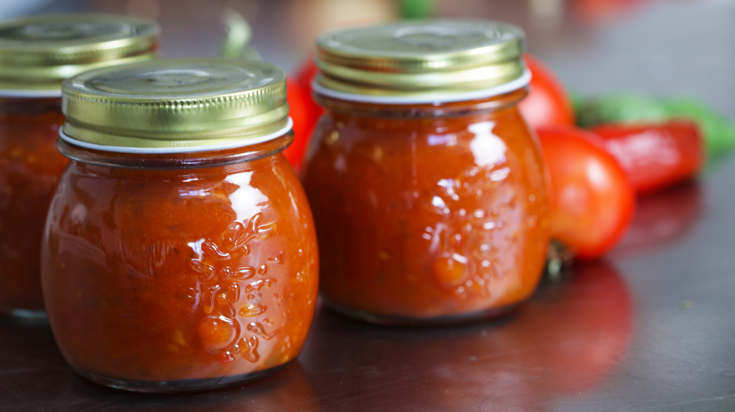 Three jars of tomato chutney on a table with the tomatoes