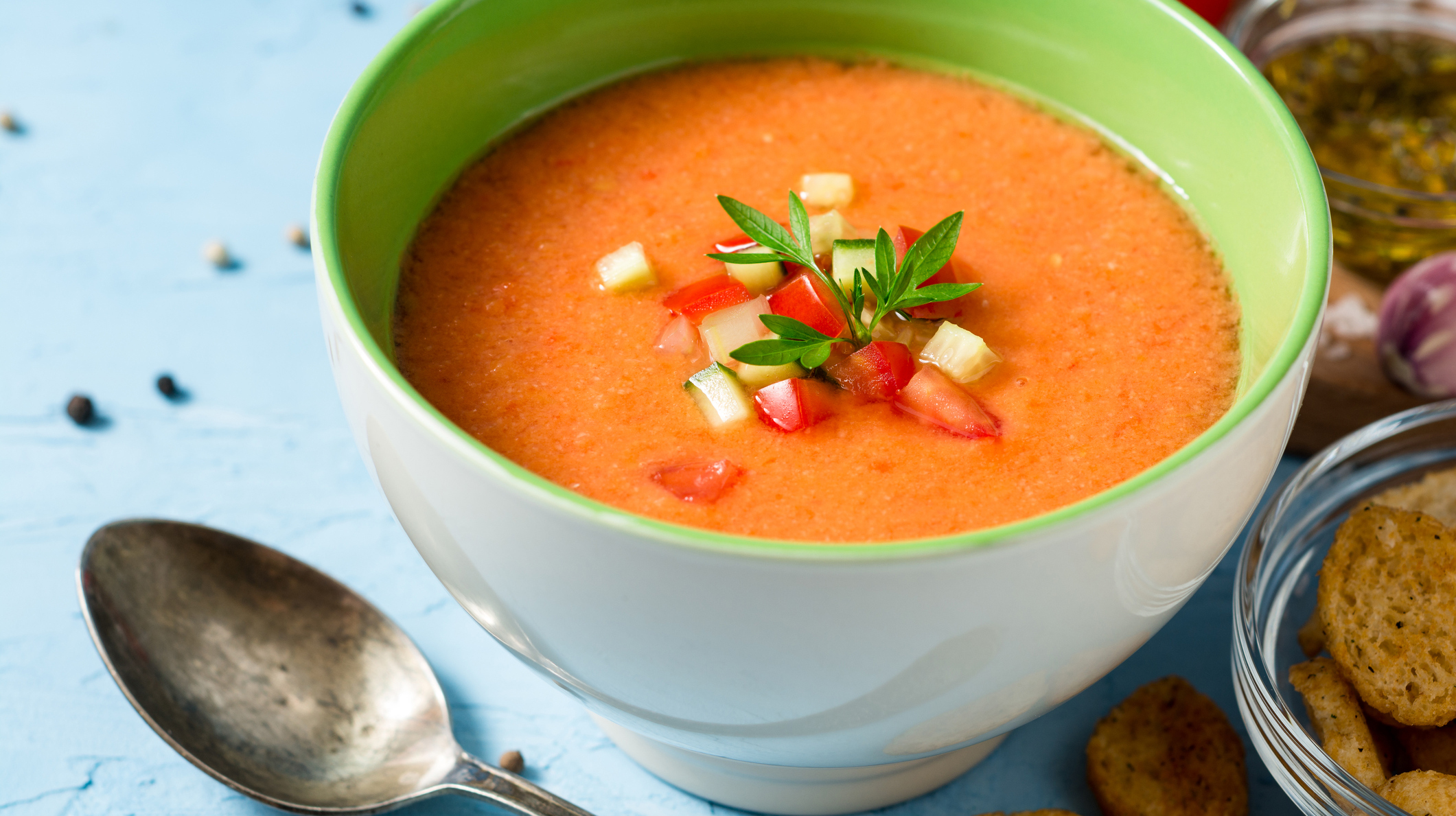 Summer cold soup gazpacho with parsley and vegetables on blue concrete background.