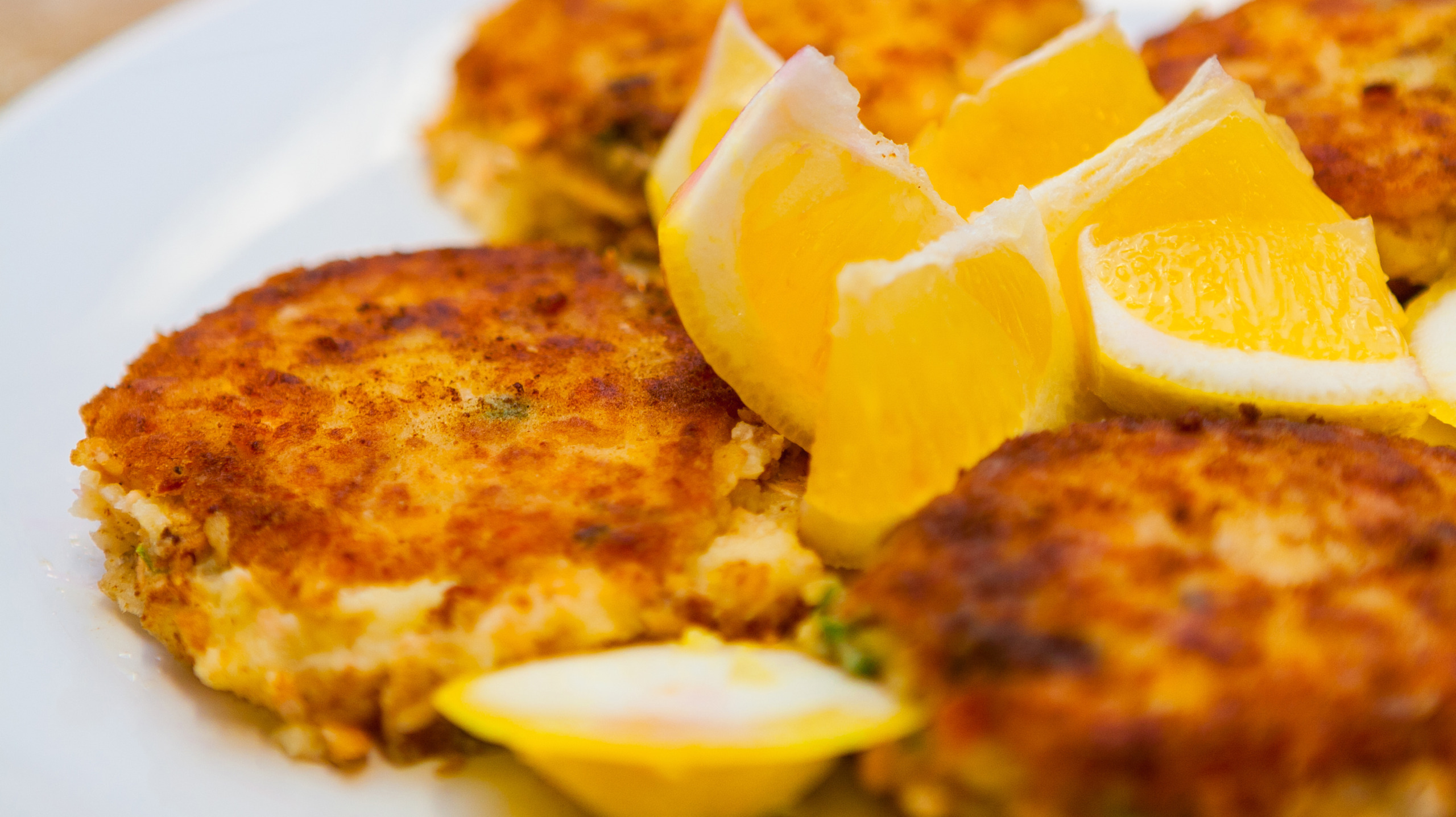 Closeup of Crispy Crab and Fish Cakes with Lemon Wedges on a White Plate