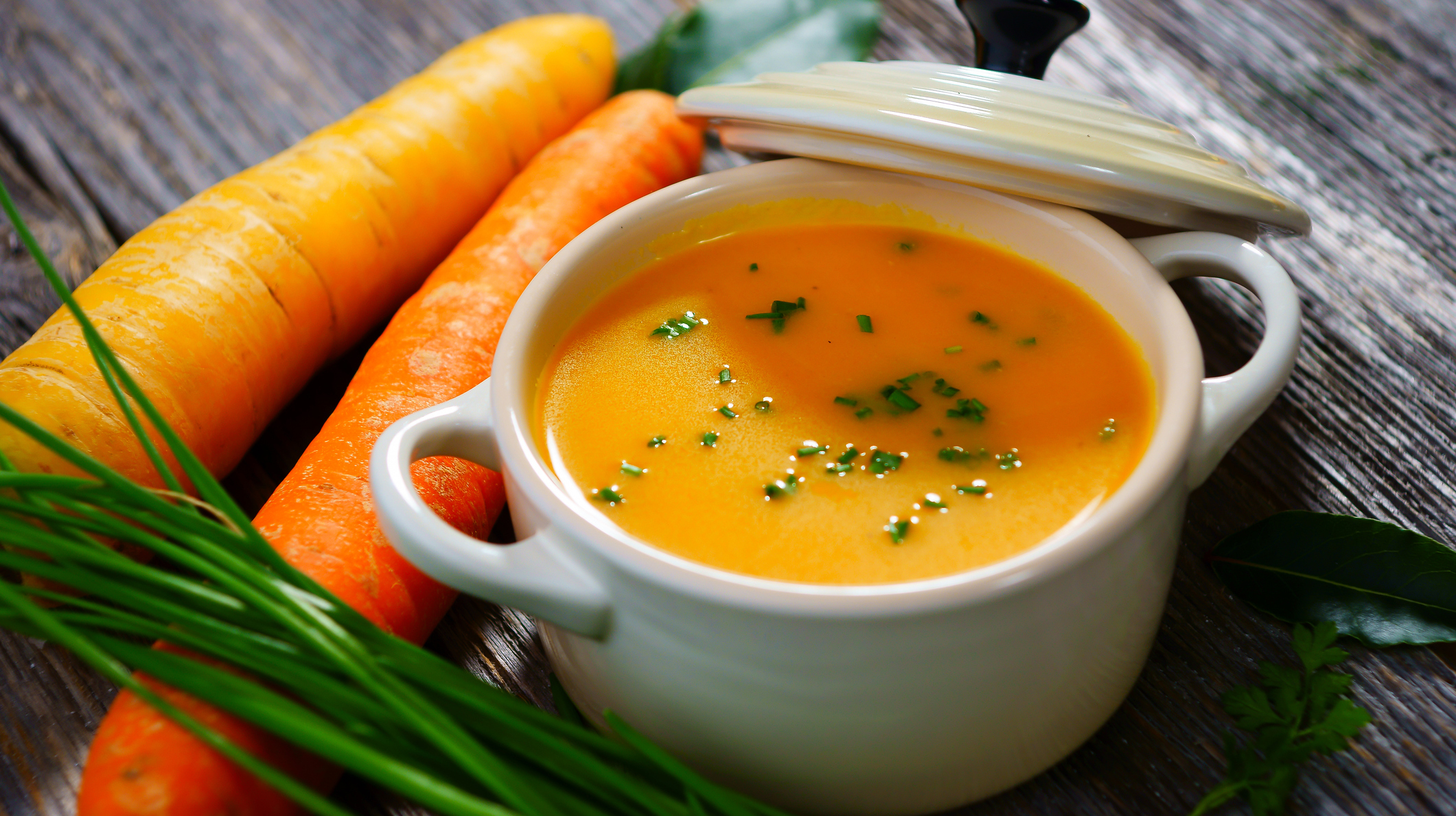 Carrot soup in a white bowl with lid and carrots on the side