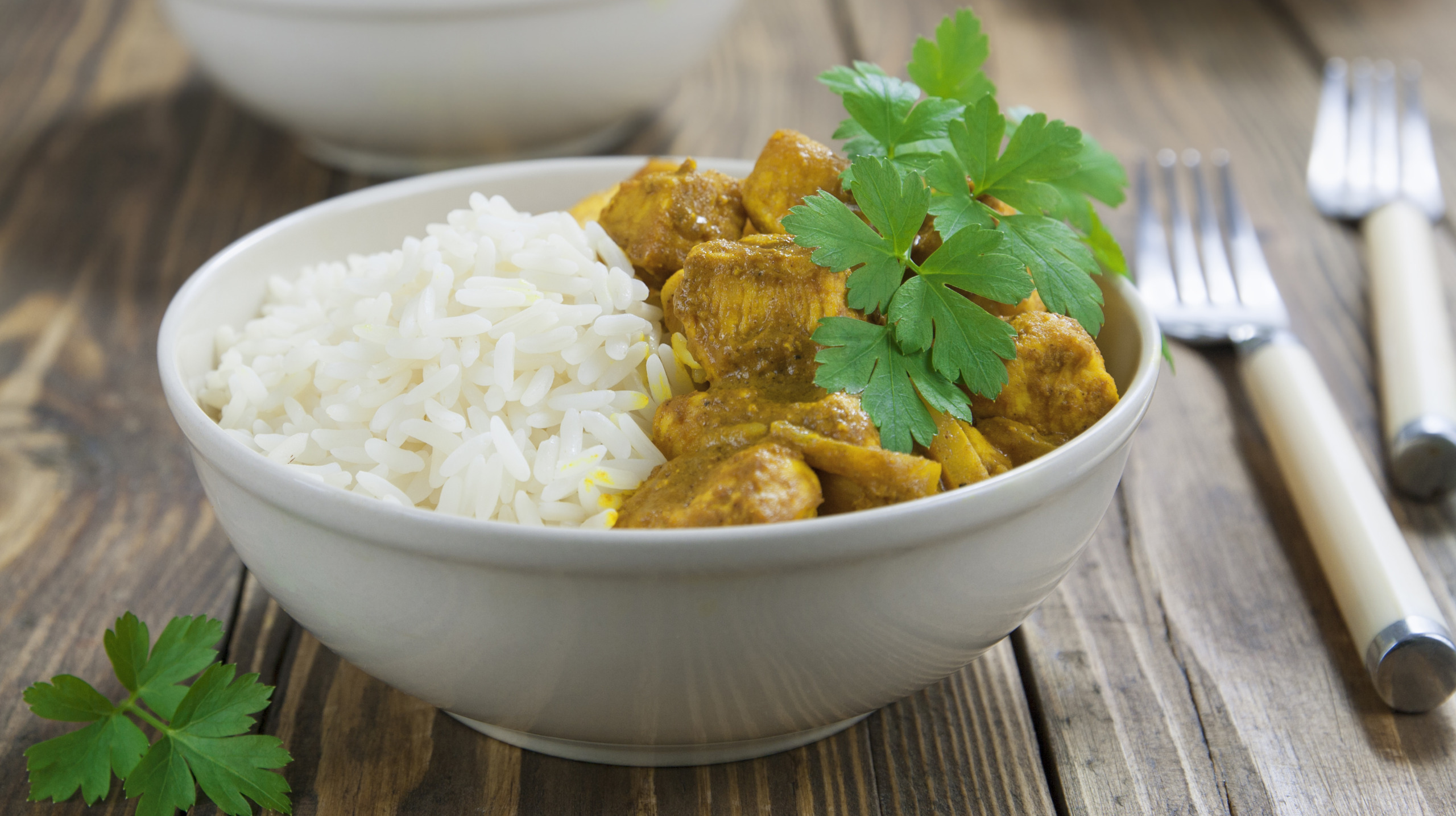 White bowl of chicken curry with rice on wooden table