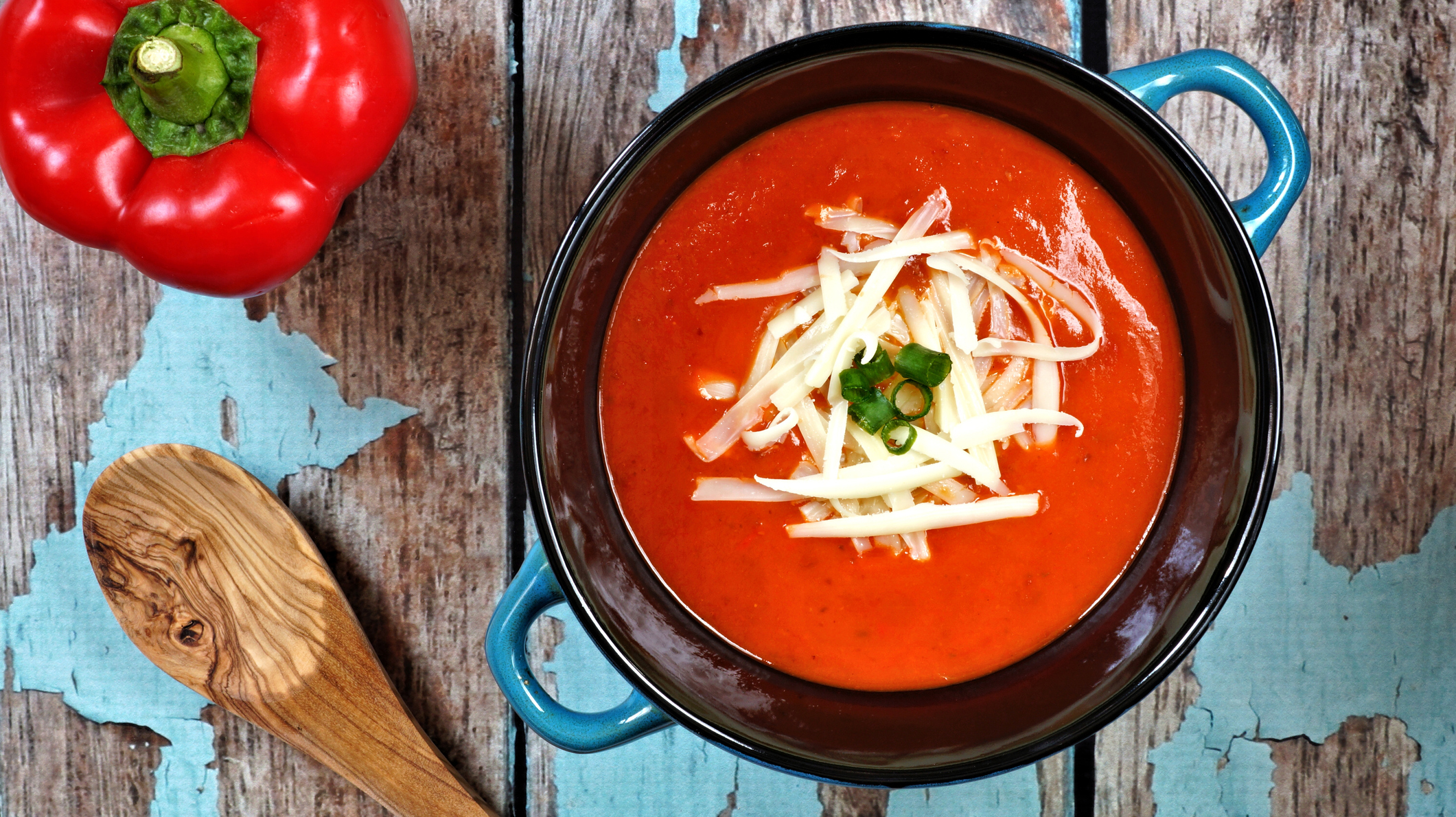 Red pepper soup overhead scene on rustic blue wood background
