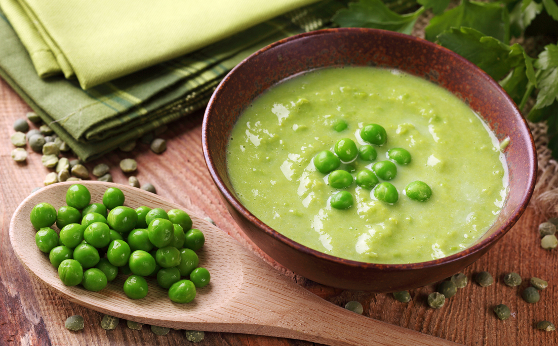 A bowl of green pea soup with a wooden spoon