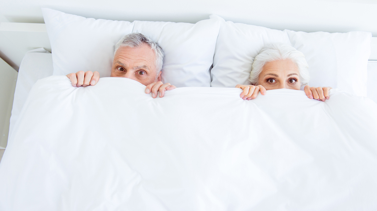 High angle top view surprised funny couple gray hair people in pajama, sleep, wear, sleepwear, nightwear with big eyed lying in the bed linen, sheets hiding themselves under blanket