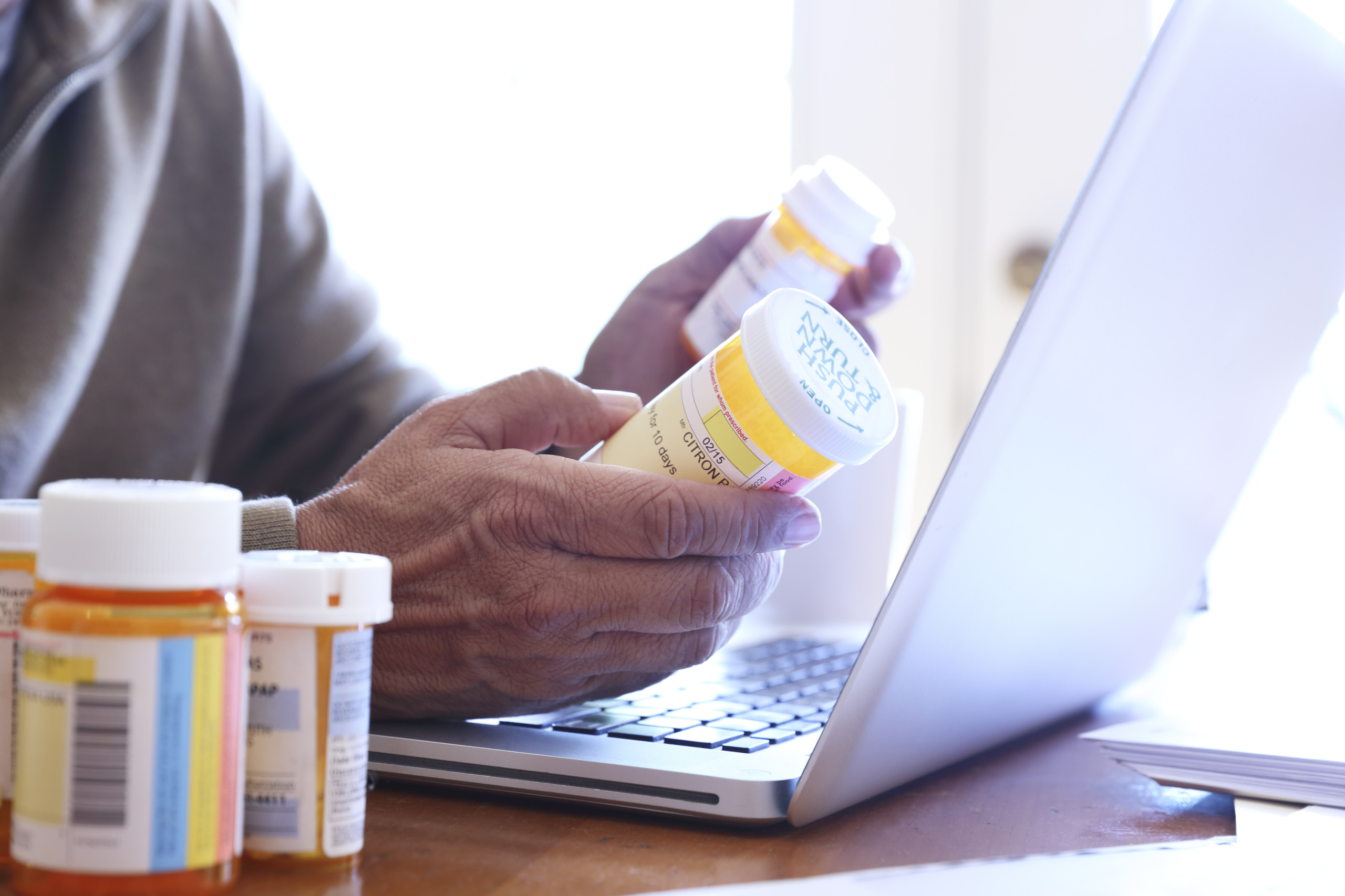 Close up Of Man Holding Prescription Medication Bottles In Front Of Laptop