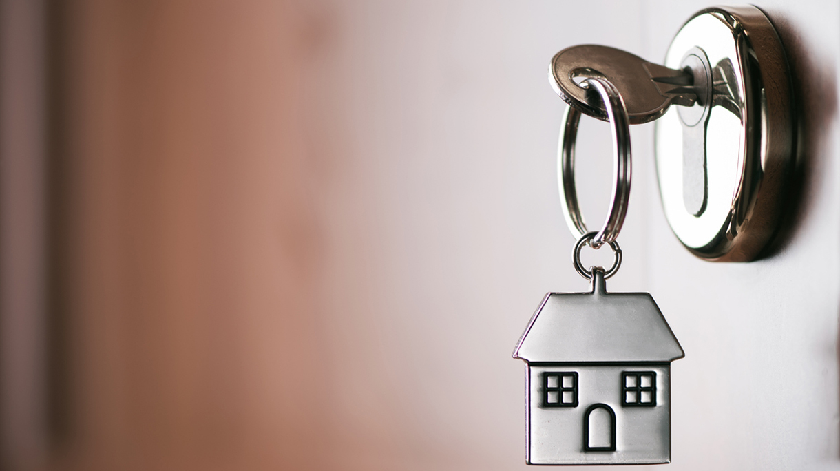 House key on a house shaped silver keyring in the lock of a entrance  brown door
