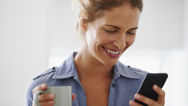 Woman drinking coffee using smartphone at home