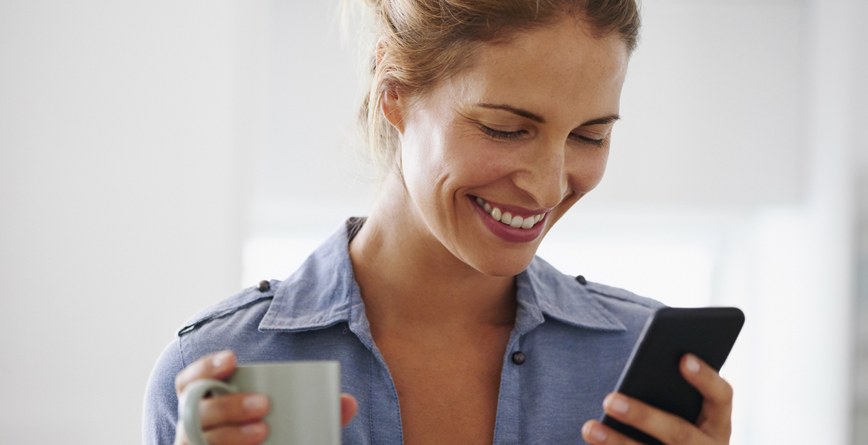Woman drinking coffee using smartphone at home