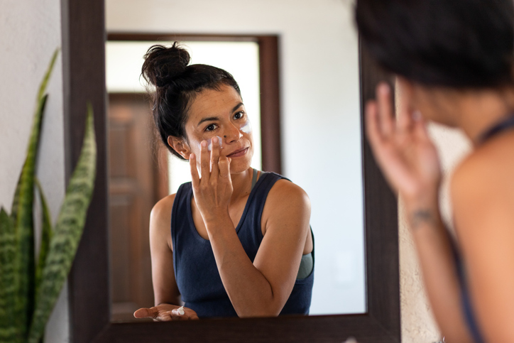 Vrouw smeert zich voor de spiegel in met zonnebrandcreme op haar gezicht