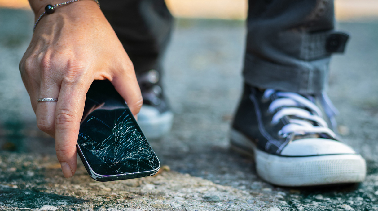 Woman picking up broken smartphone from the ground.