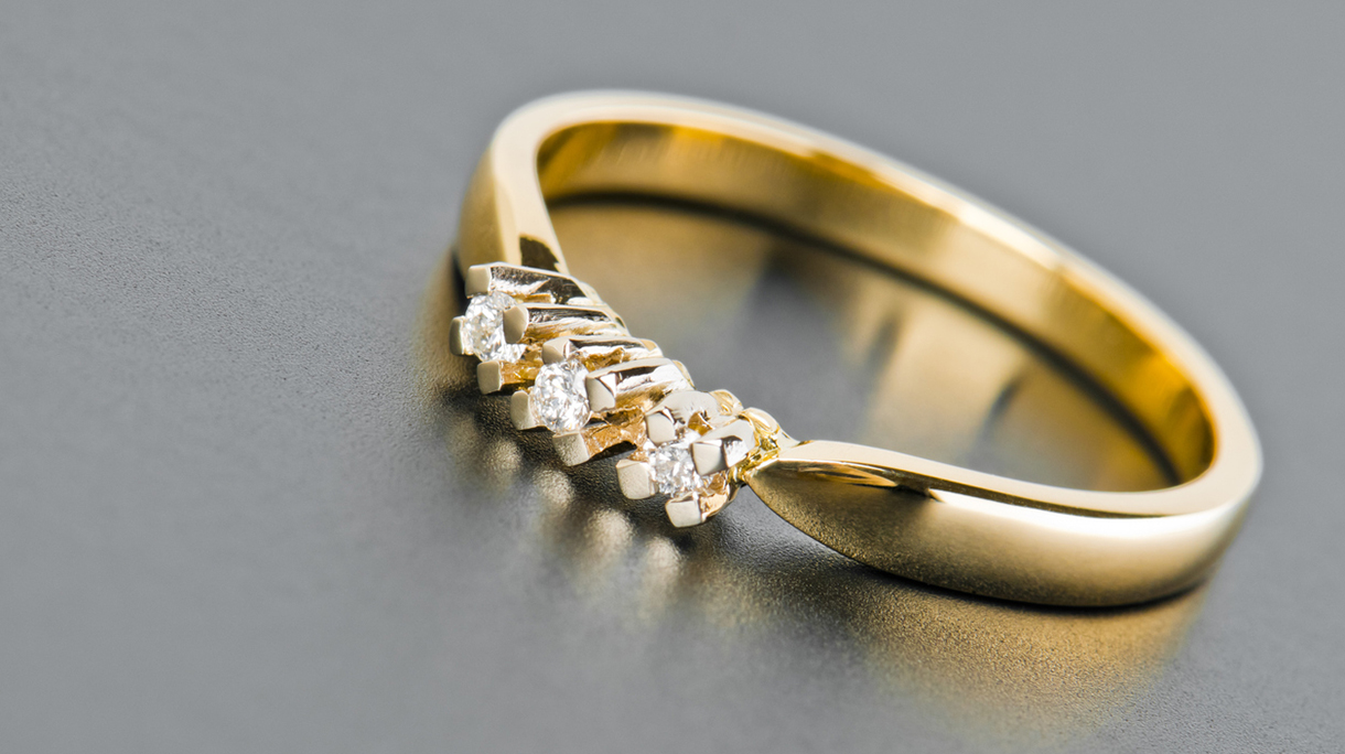 Close-up of single golden ring with diamonds against solid gray