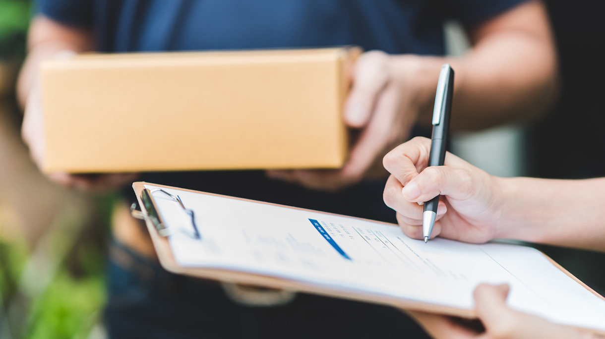 Hand putting signature in clipboard to receive package from delivery man