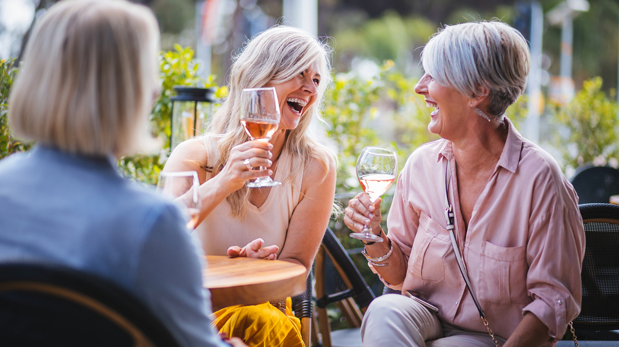 Happy senior women drinking wine and laughing together at restaurant
