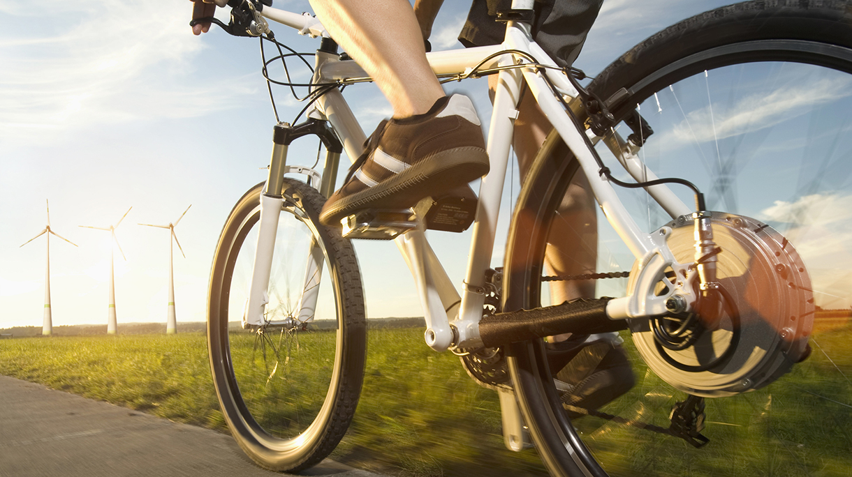 “Low section of mature man riding electric bicycle with wind turbine at sunset, Bavaria, Germany”