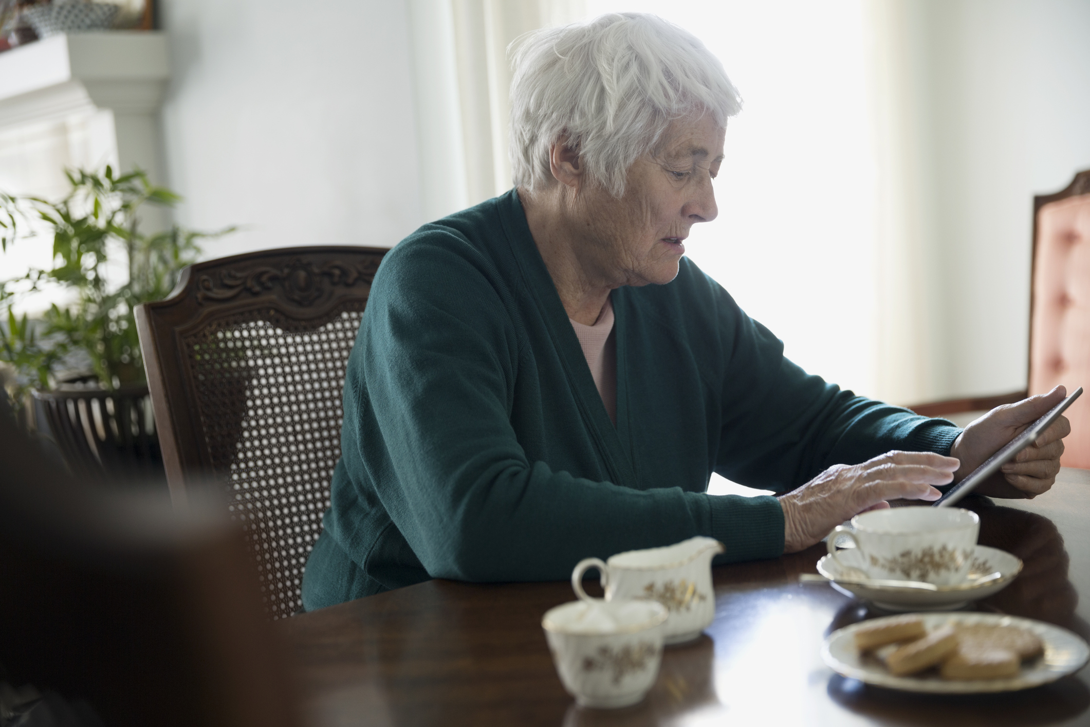 Senior woman drinking tea and using digital tablet at dining table