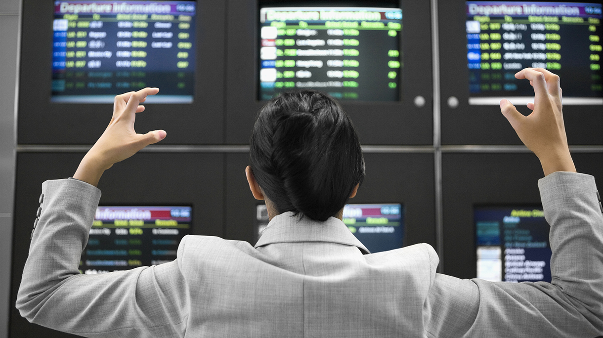 Rear view of a businesswoman looking angry in front of an arrival departure board at an airport