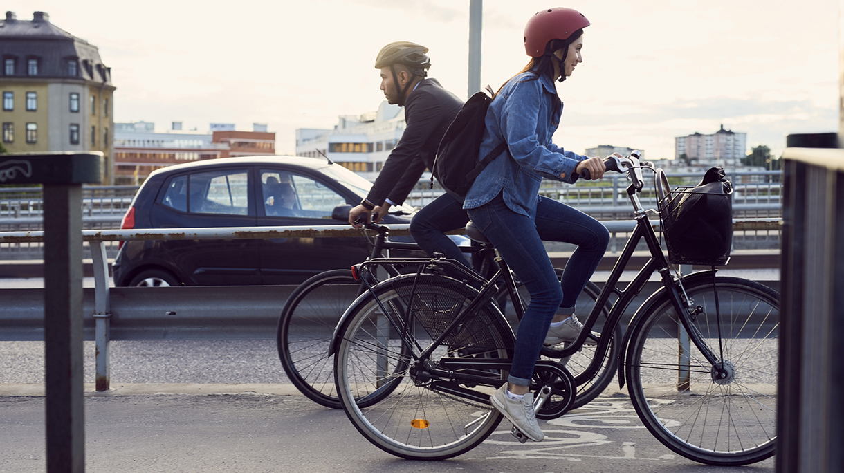 Side view of people cycling on street against sky