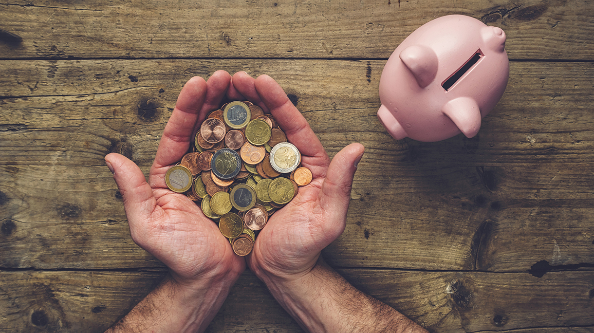 Directly Above Shot Of Hands Holding Coins By Piggy Bank On Table