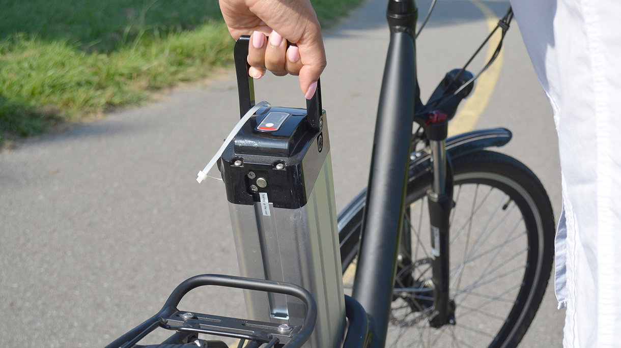 Women holding battery pack of electric bicycle near her e bike. Female taking out e bike battery. Ecology concept. Charging batteries. Renewable energy.