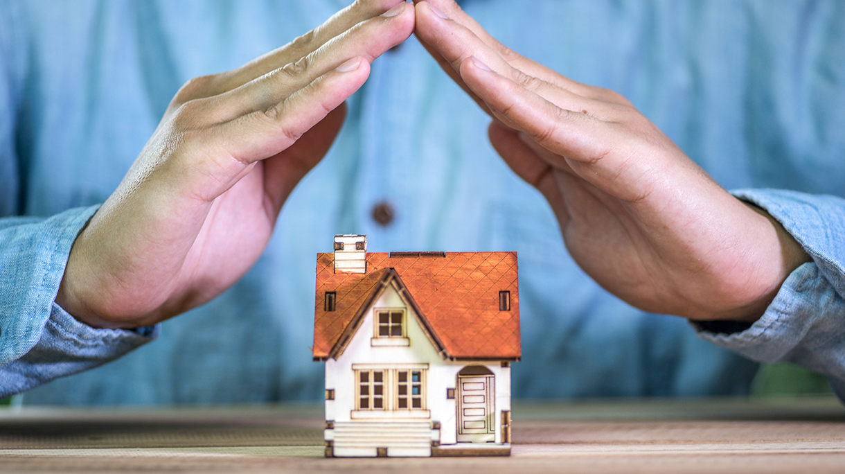 Hands covering a toy house. Home protection concept