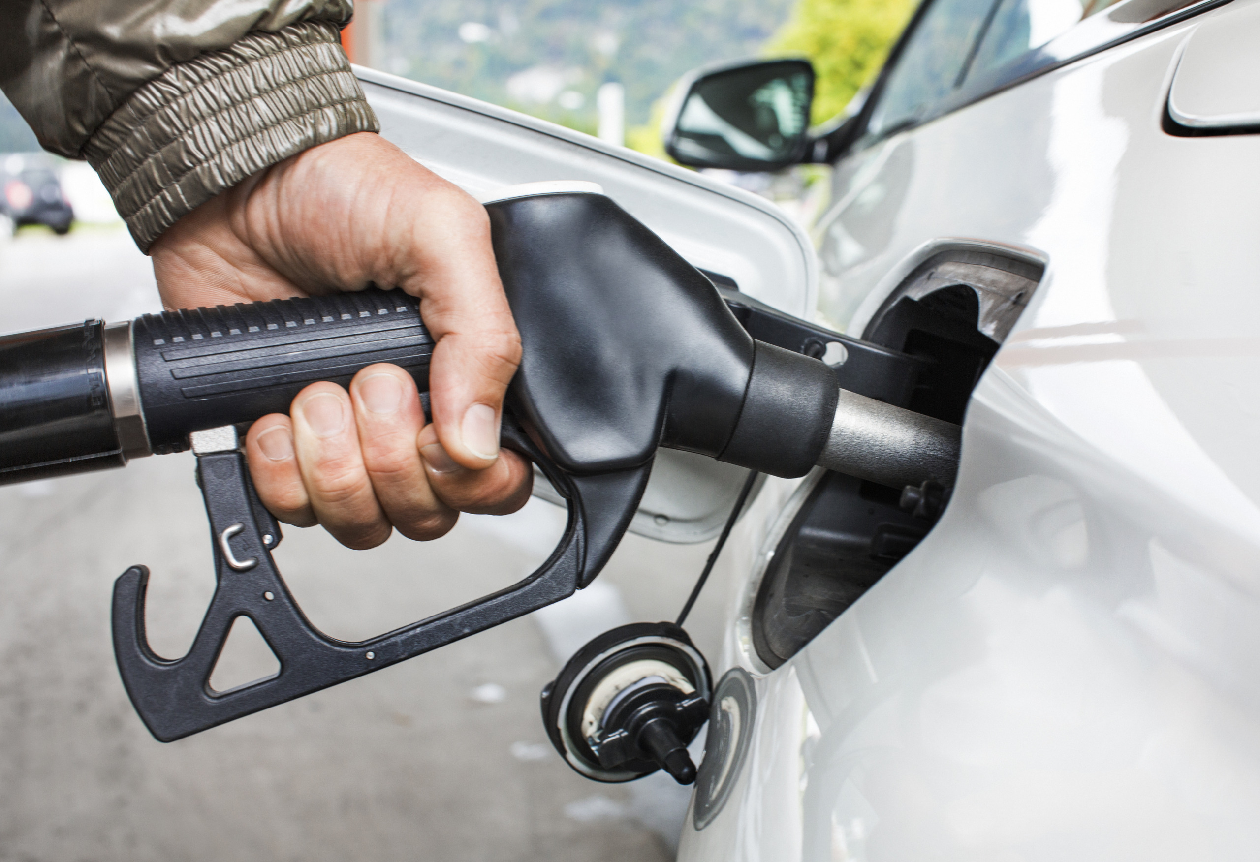 Mans’s hand holding fuel nozzle in car