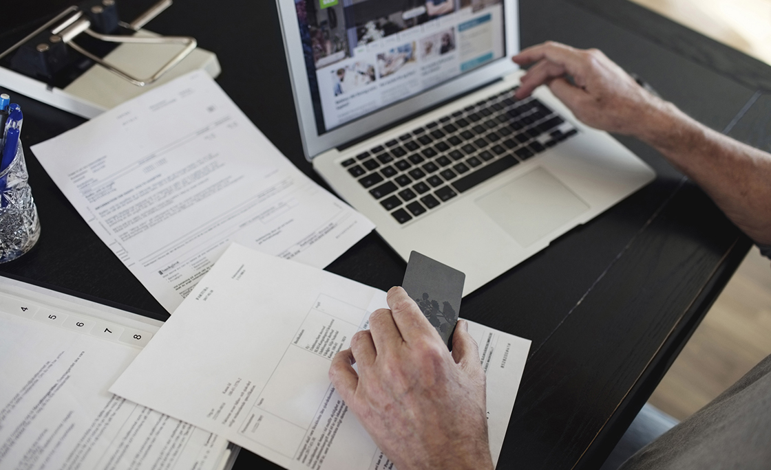 Cropped image of senior man with bills doing online payment at home