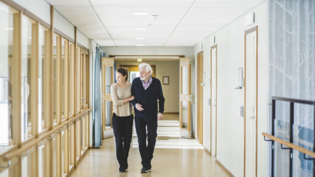 Young woman looking away while walking with grandfather in corridor at nursing home