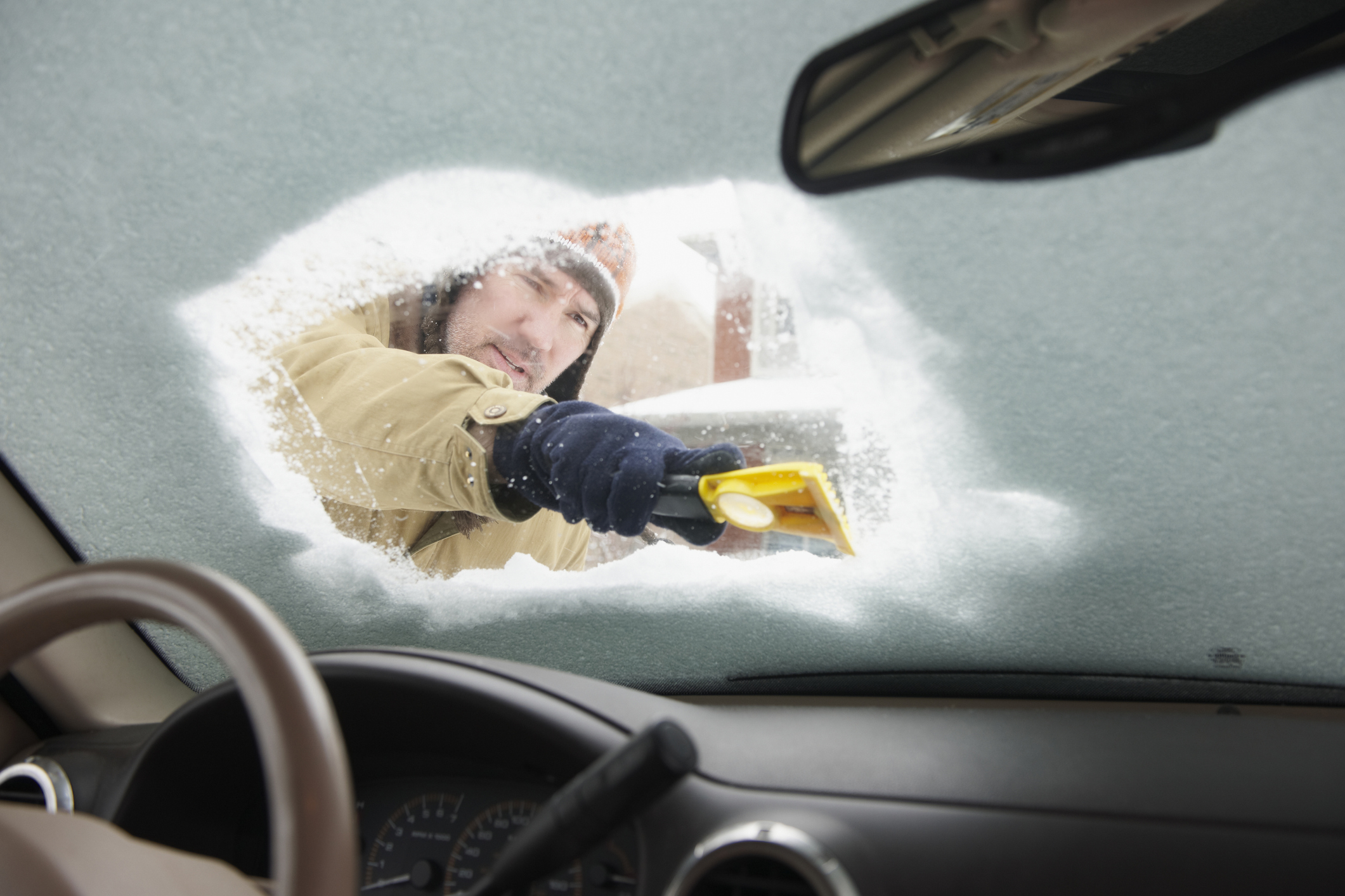 Caucasian man scraping snow off car windshield