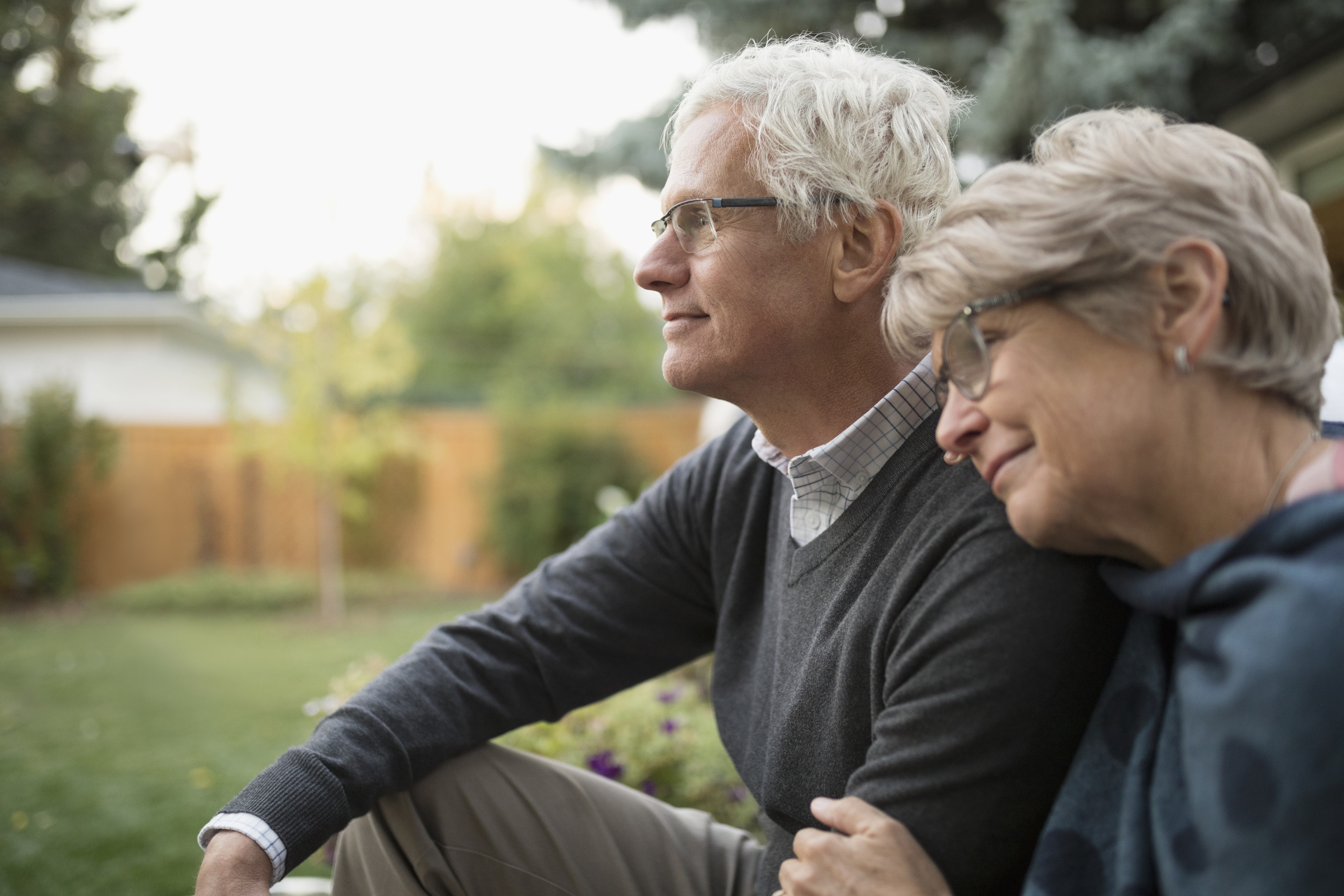 Affectionate senior couple hugging, looking away in backyard