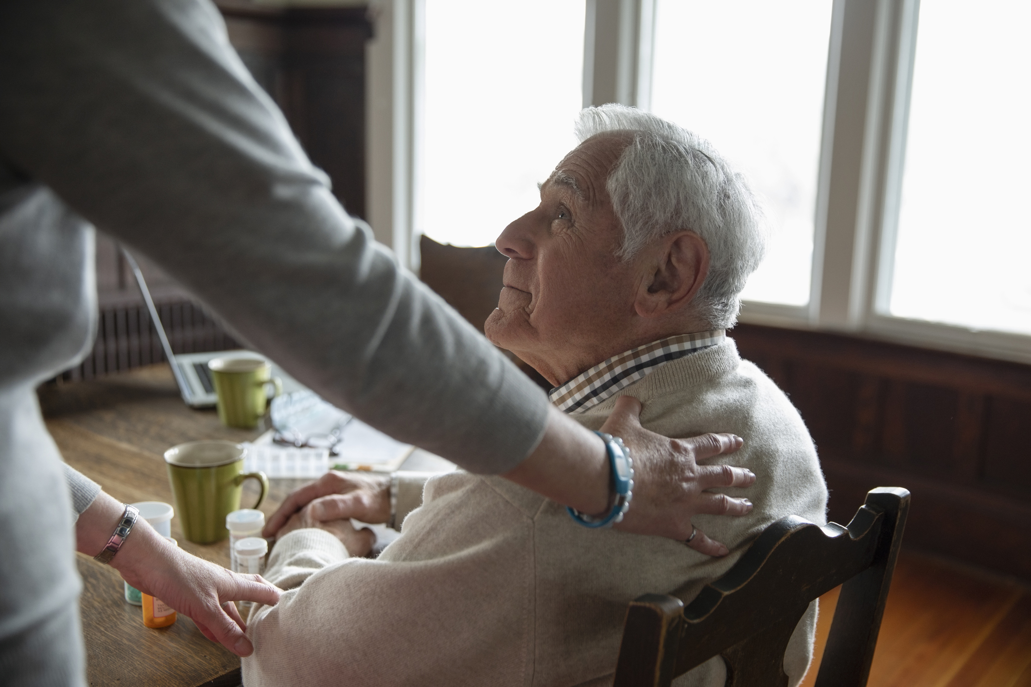Home caregiver comforting senior man at table