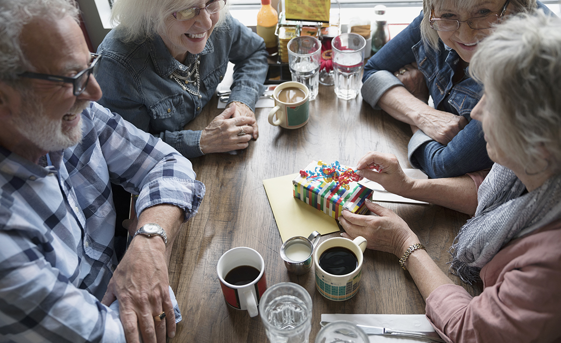 Senior friends celebrating birthday, opening gift in diner