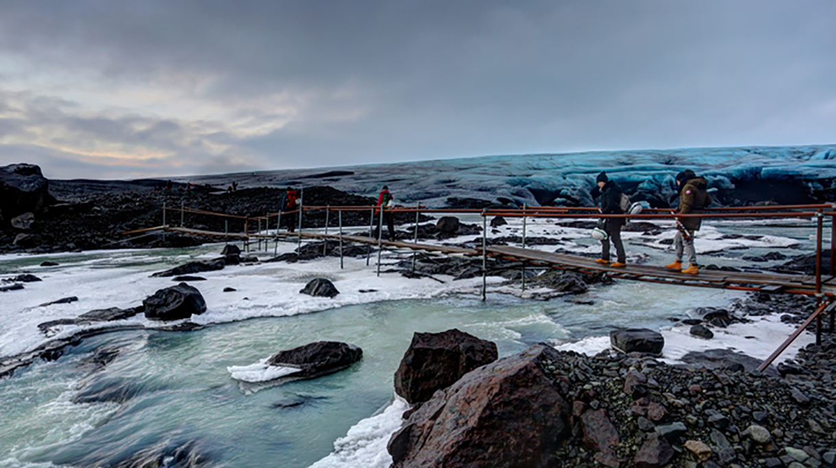 Hikers crossing glacier melting water on a footbridge