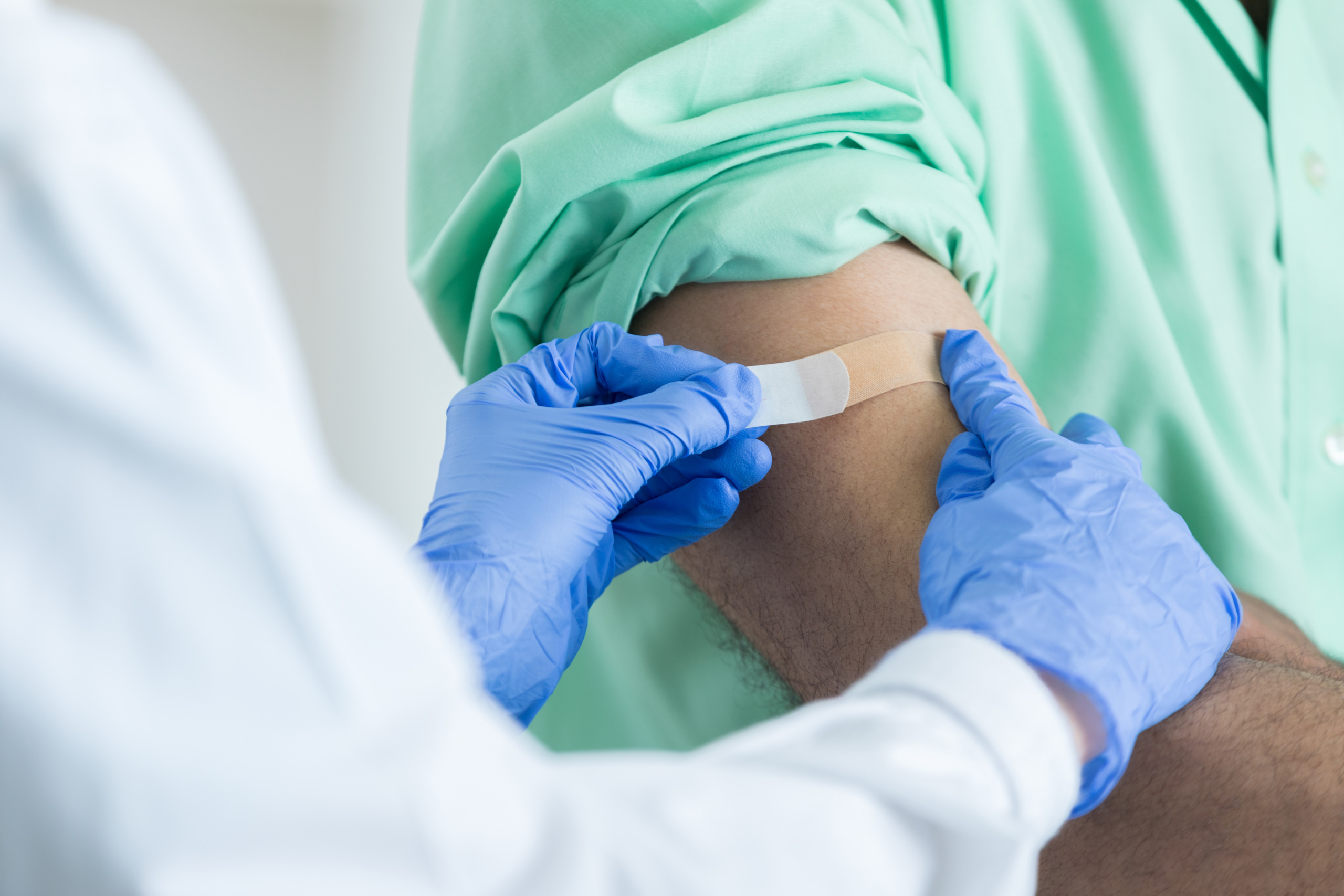 Closeup of unrecognizable pharmacist placing bandaid on customer’s arm