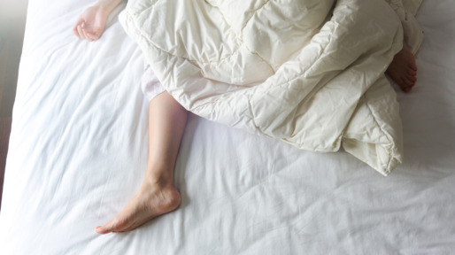 Bare Feet of a Young Woman on White Bed