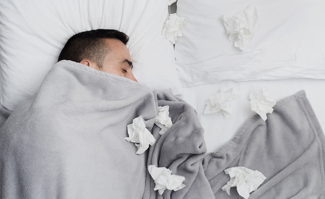 ill man in bed surrounded by used tissues