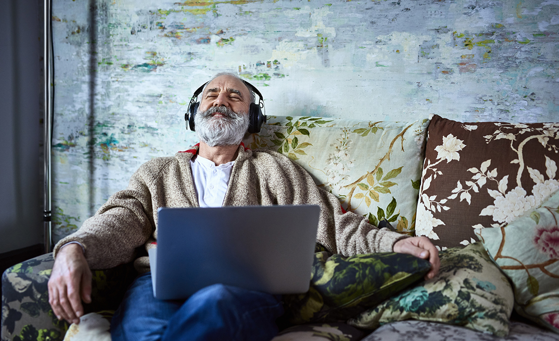 Portrait of mature man on sofa smiling and wearing headphones