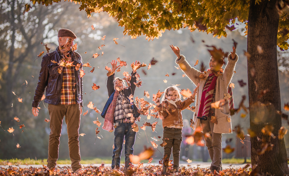 Playful grandparents and their grandkids having fun while throwing autumn leaves in nature.