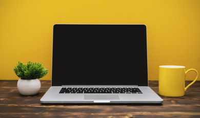 Laptop and Yellow Coffee Mug on Office Desk Against Yellow Background
