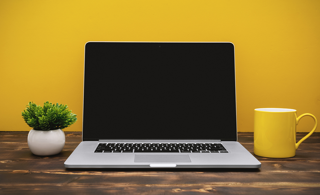 Laptop and Yellow Coffee Mug on Office Desk Against Yellow Background