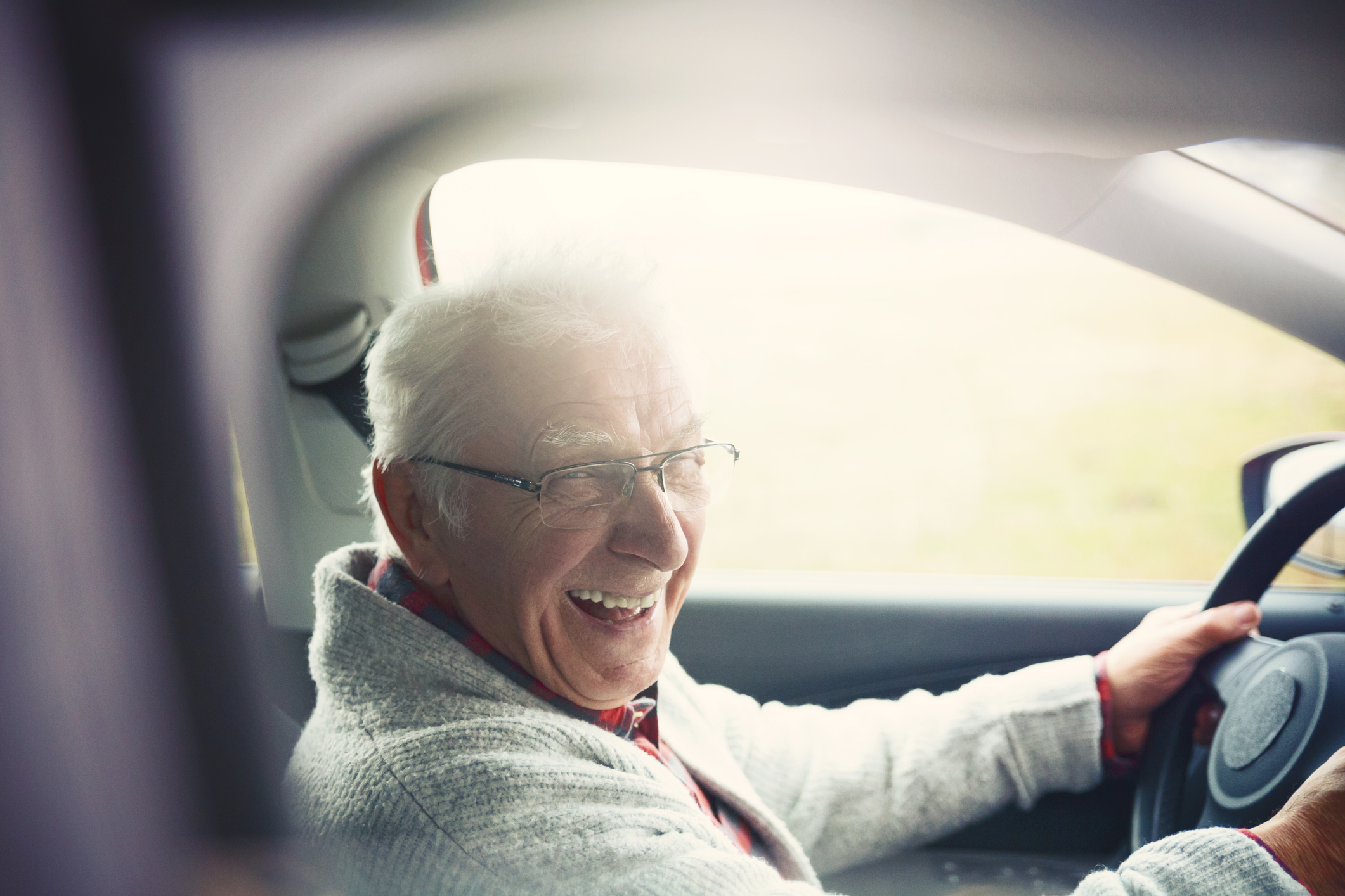 Old gentleman drives car and laughs at the camera