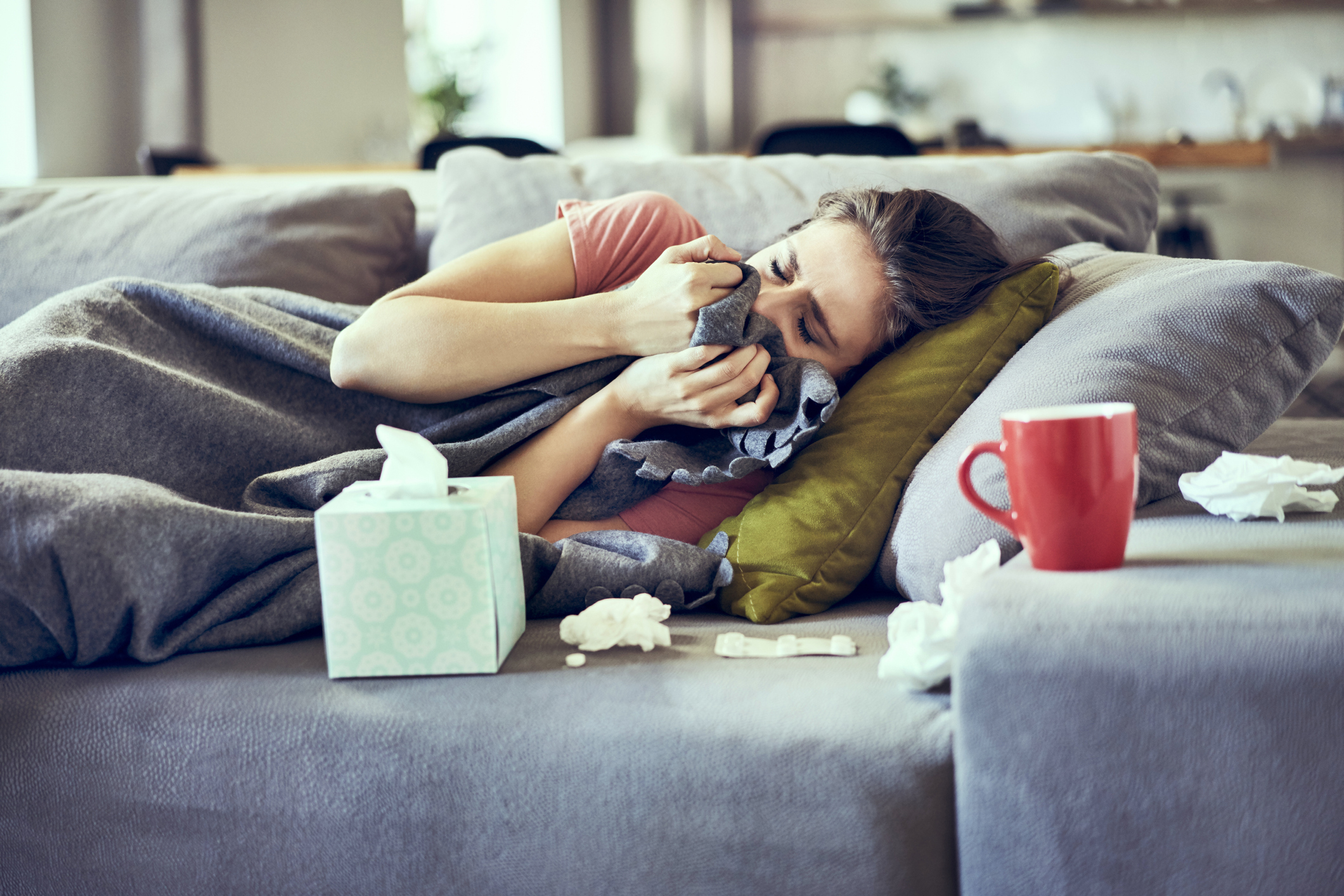 Sick woman trying to take a nap while lying on couch covered in blanket