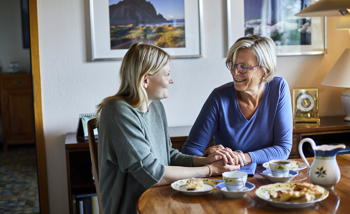 Senior woman and young woman sitting at dining table holding hands